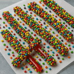 A colorful tray of homemade cannabis-infused nerd ropes, glistening with candy pieces on a parchment paper surface.